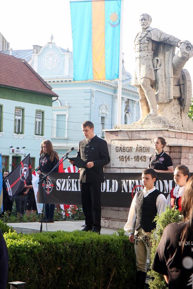 Membrii HVIM la o manifestare publică în centrul municipiului Târgu Secuiesc, unde primar este UDMR-istul Bokor Tibor. Tinerii țin un baner pe care se poate citi ”ținutul secuiesc nu e România” 